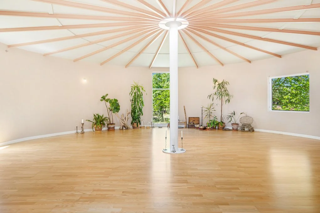 Spacious room with wooden floor, white walls, plants, and a circular ceiling design with wooden beams.