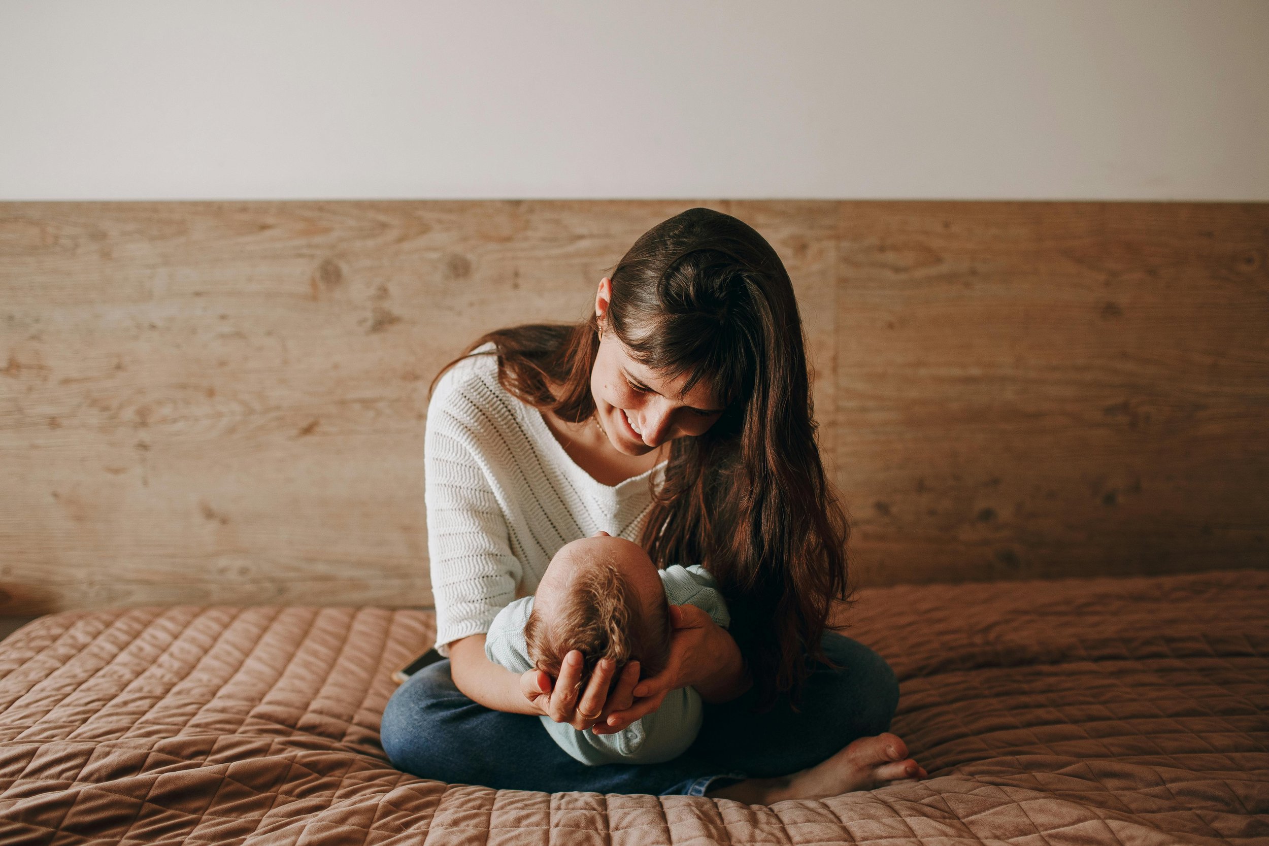 Mother sitting on bed holding baby, highlighting postpartum support, breastfeeding guidance, and lactation counseling for new moms in Orlando area.