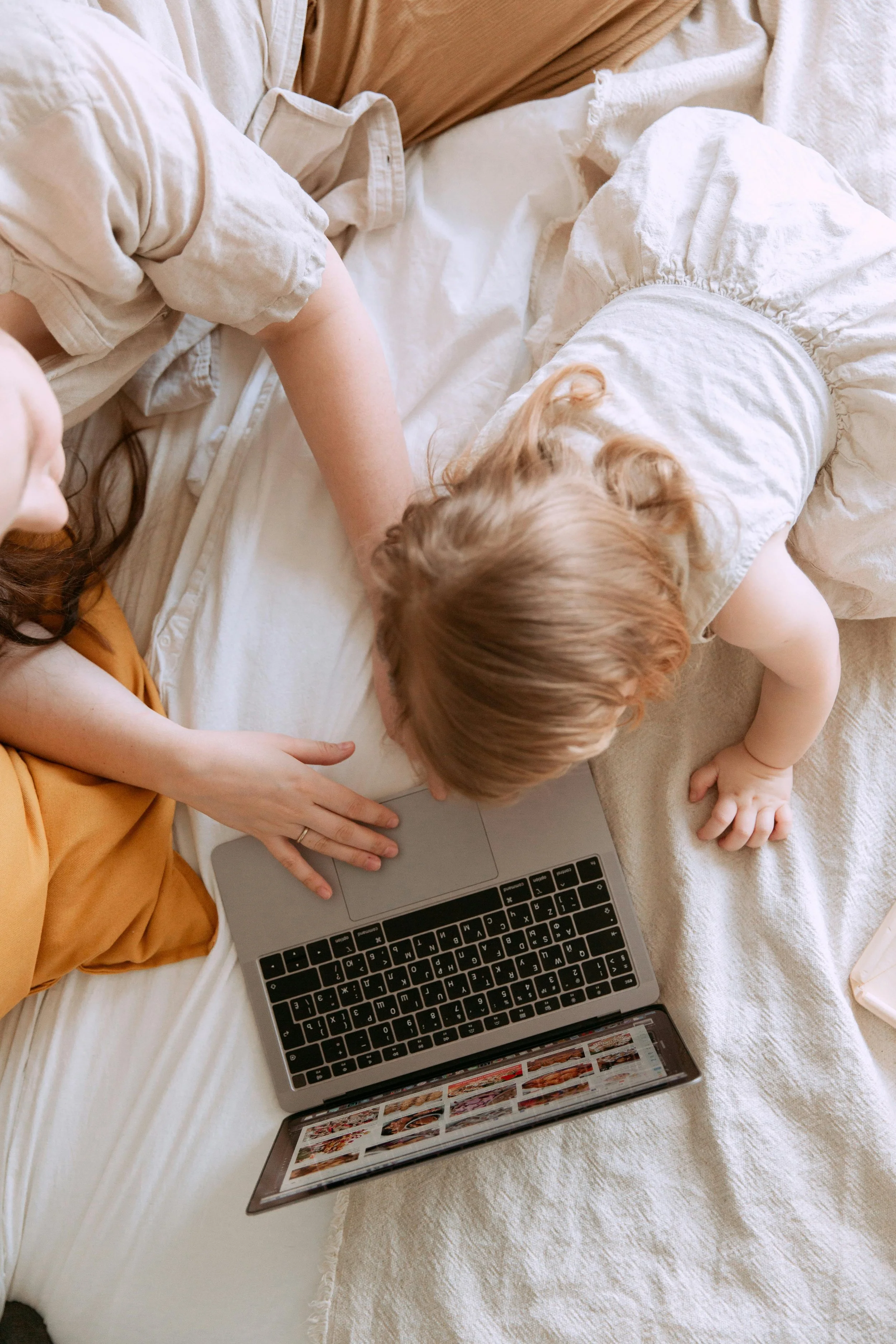 Mother and child bonding on bed while using laptop, representing virtual lactation counseling and breastfeeding support for new families in Winter Garden and Horizon West.