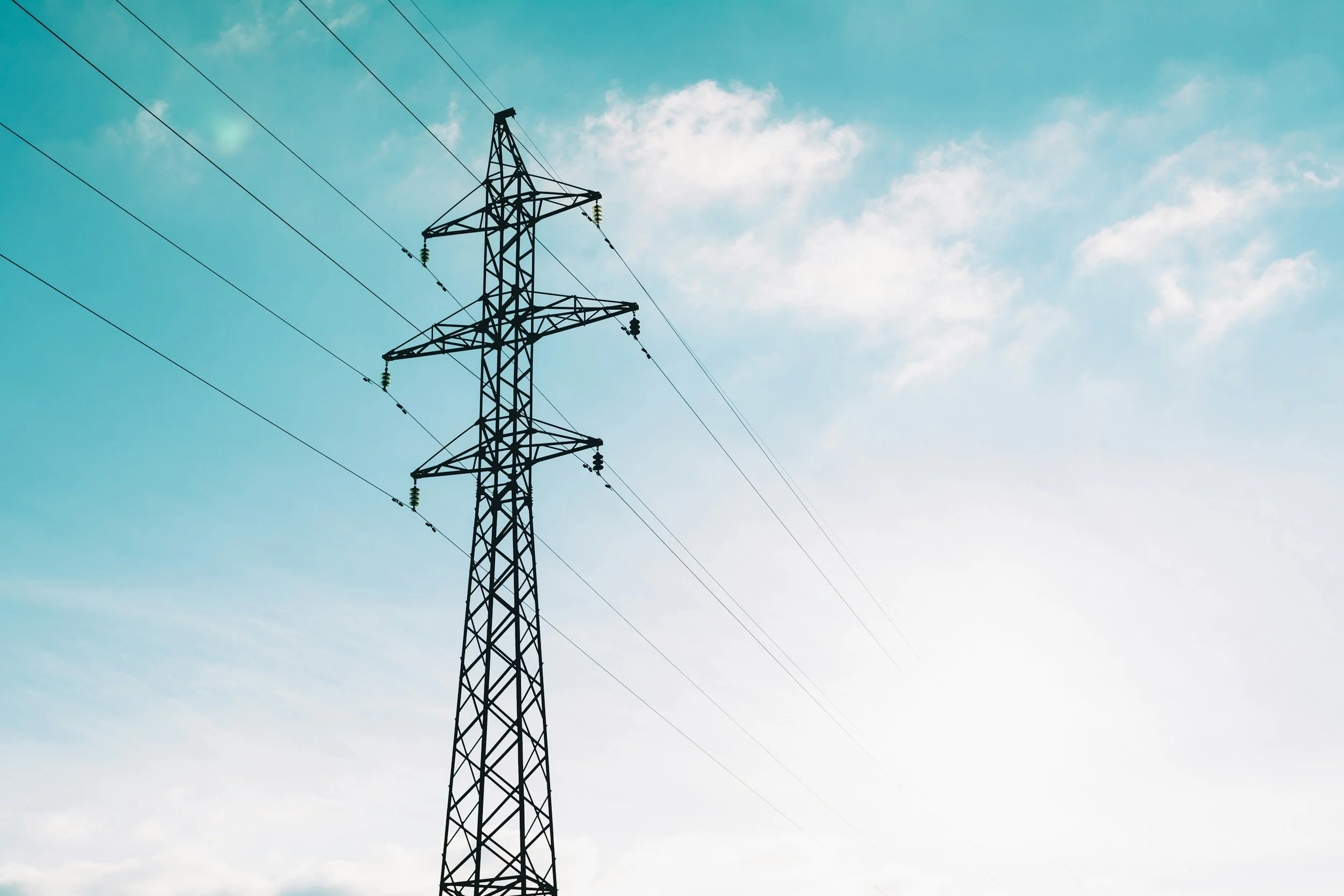A tall electricity pylon against a bright sky with some clouds.
