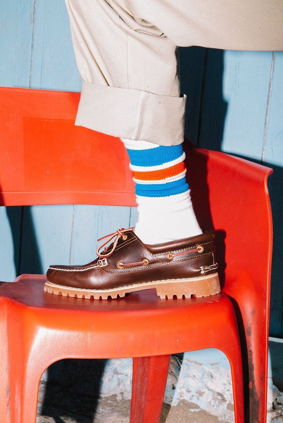 Scarpa marrone in pelle con suola spessa, indossata con calzini multicolori, appoggiata su una sedia rossa.