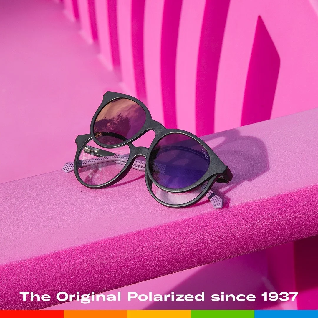 Occhiali da sole su una superficie rosa, con sfondo rosa tratteggiato, riflessi nelle lenti