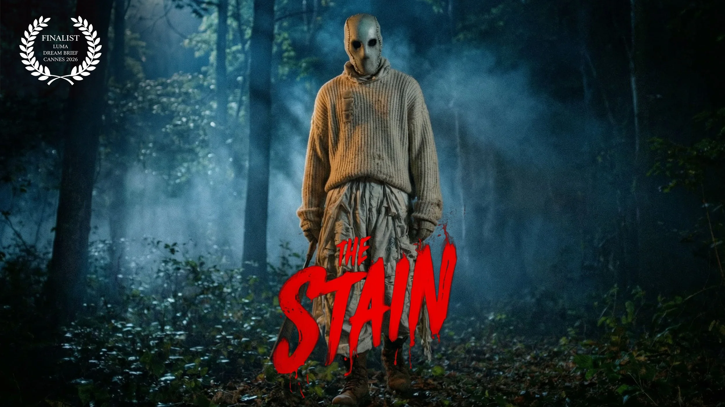 A person wearing a mask and a oversized sweater standing in a misty forest with trees in the background. The text 'The Stain' appears in red at the bottom left corner, and a white laurel wreath with the words 'Finalist Luma Dream Brief Cannes 2026' is in the top left corner.