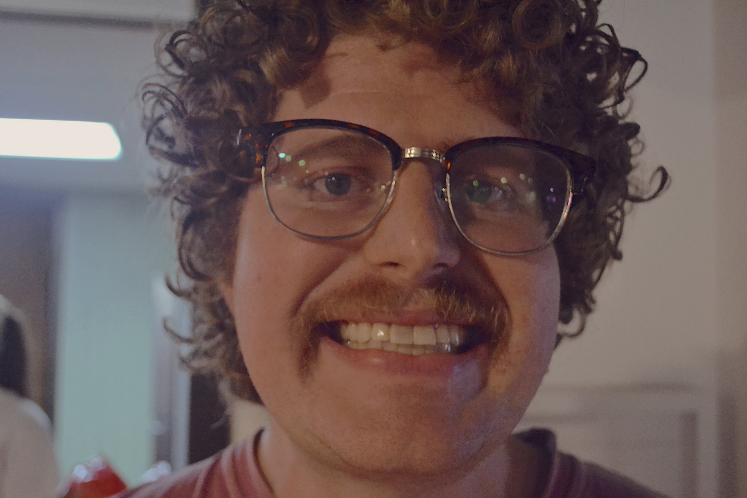 Portrait of a smiling man with curly hair and glasses, holding a green bell pepper that he grew from his garden.