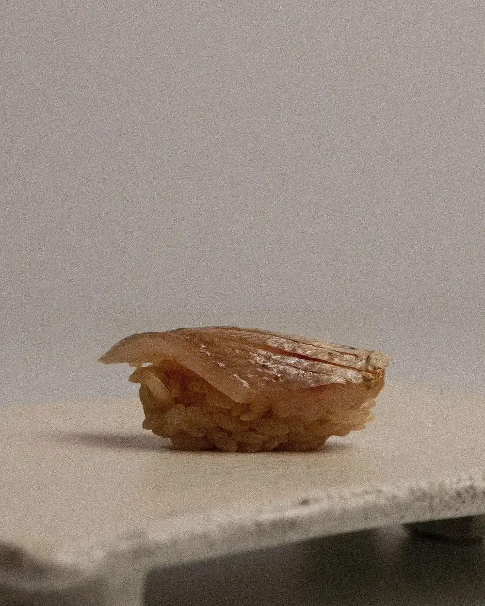 A single piece of nigiri sushi on a textured stone pedestal.