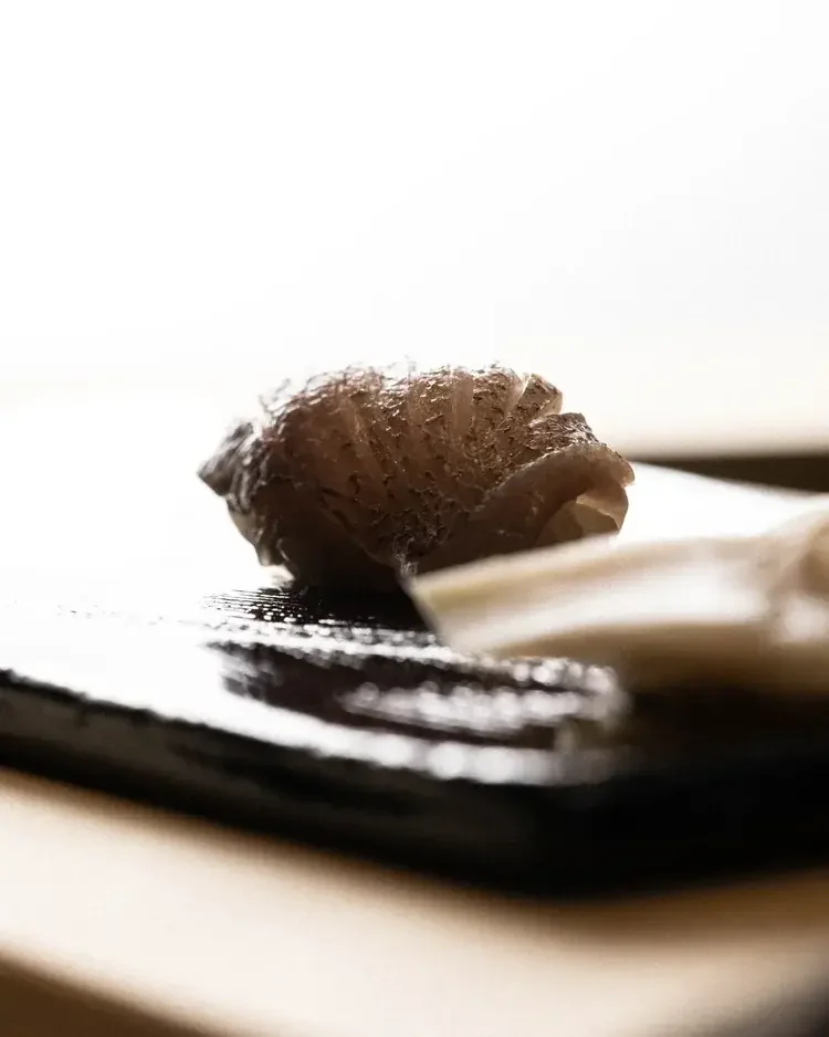 A single piece of scored silver-skinned nigiri on a black textured board.