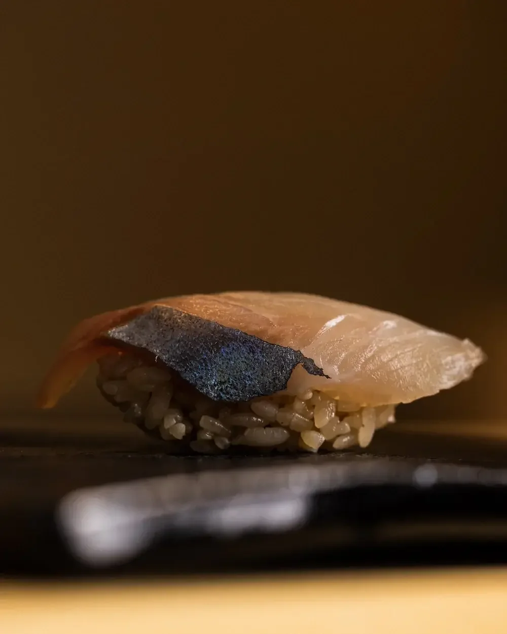 Nigiri sushi with pale fish and dark skin on a bed of rice.