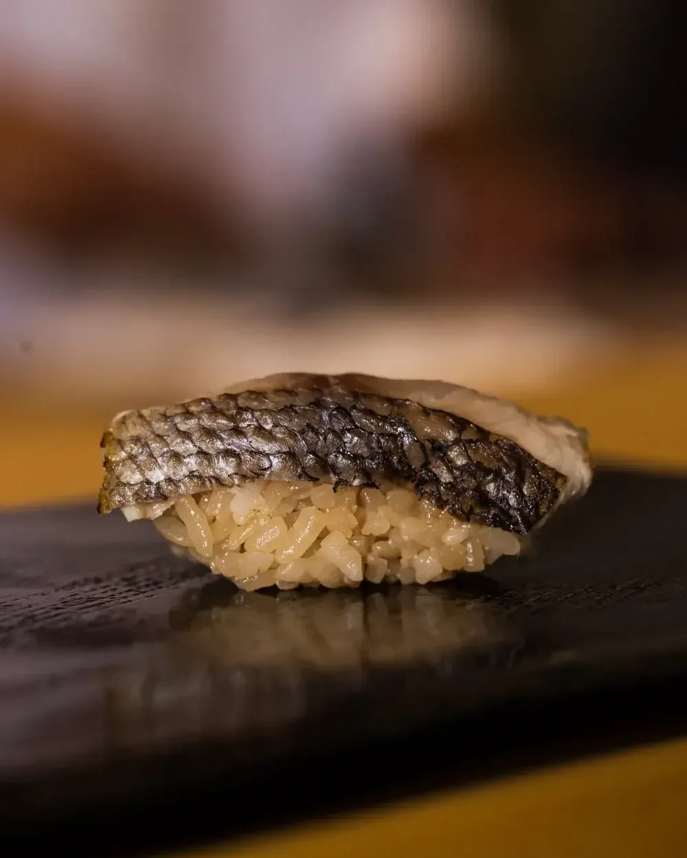 A single piece of sardine nigiri sushi with shimmering skin on a bed of rice.