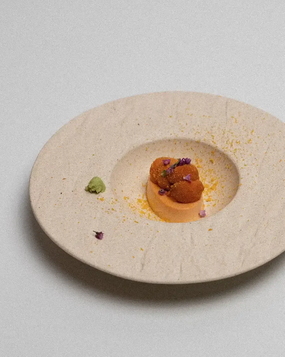 An overhead shot of a gourmet Sea Urchin (Uni) Custard on a wide, textured beige plate.