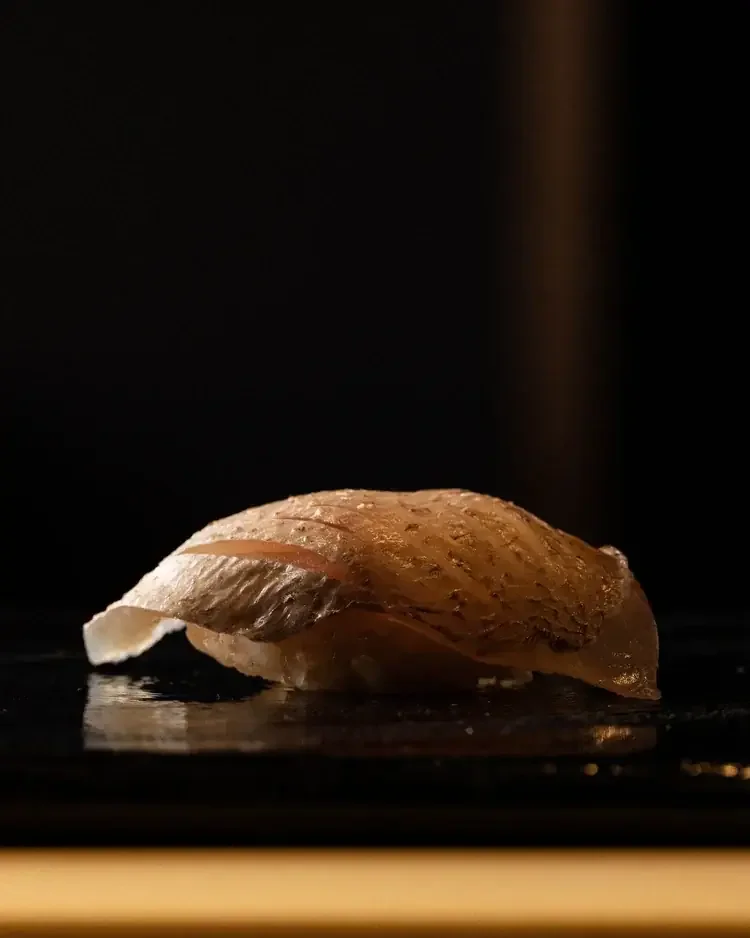 A single piece of fish nigiri on a reflective black surface.