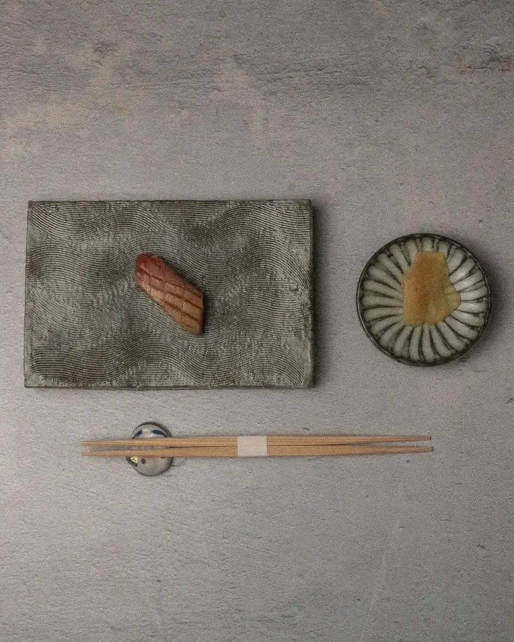 A single piece of seared nigiri sushi on a textured, rectangular slate-gray platter.