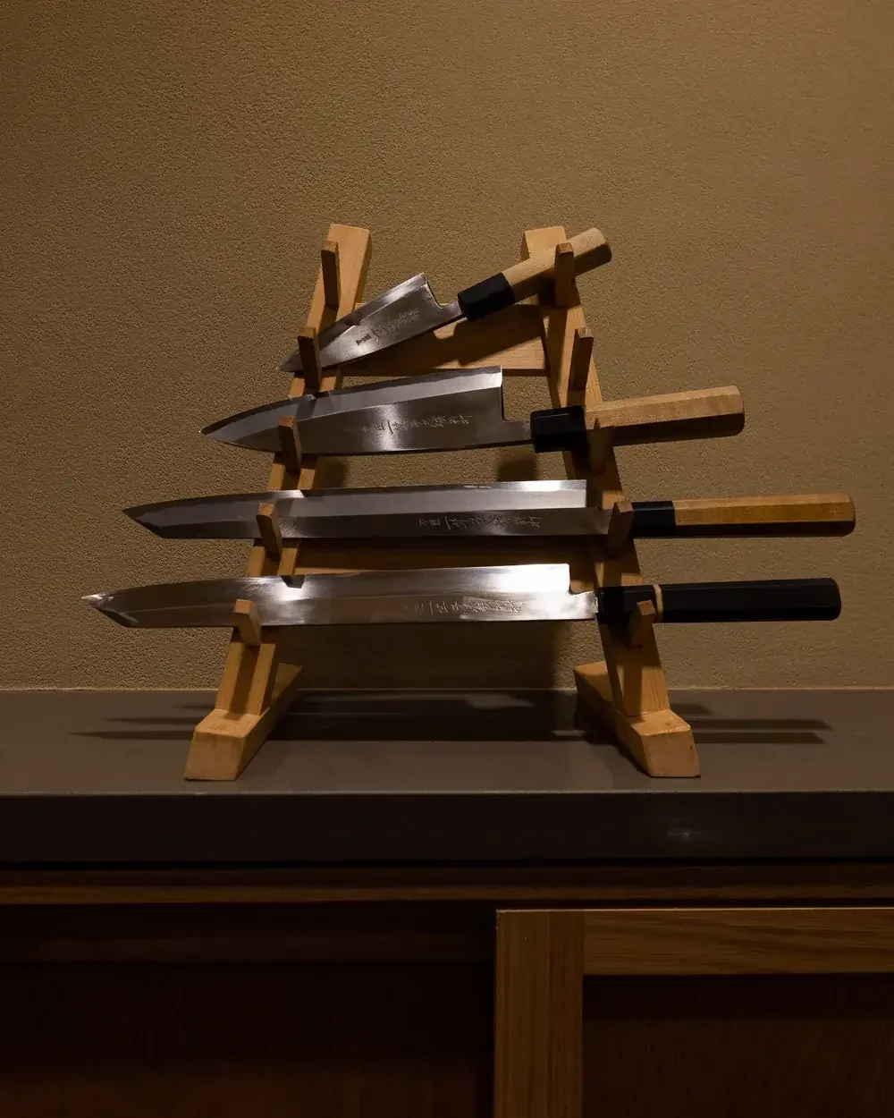 Four professional Japanese kitchen knives with wooden handles displayed on a tiered wooden rack.