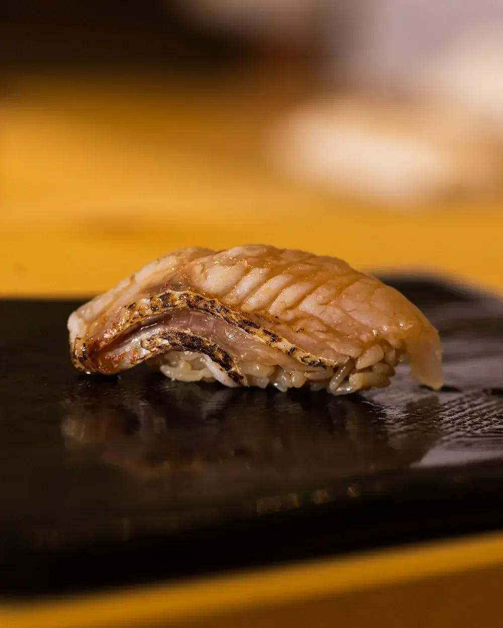 Seared nodoguro nigiri sushi on a black plate.