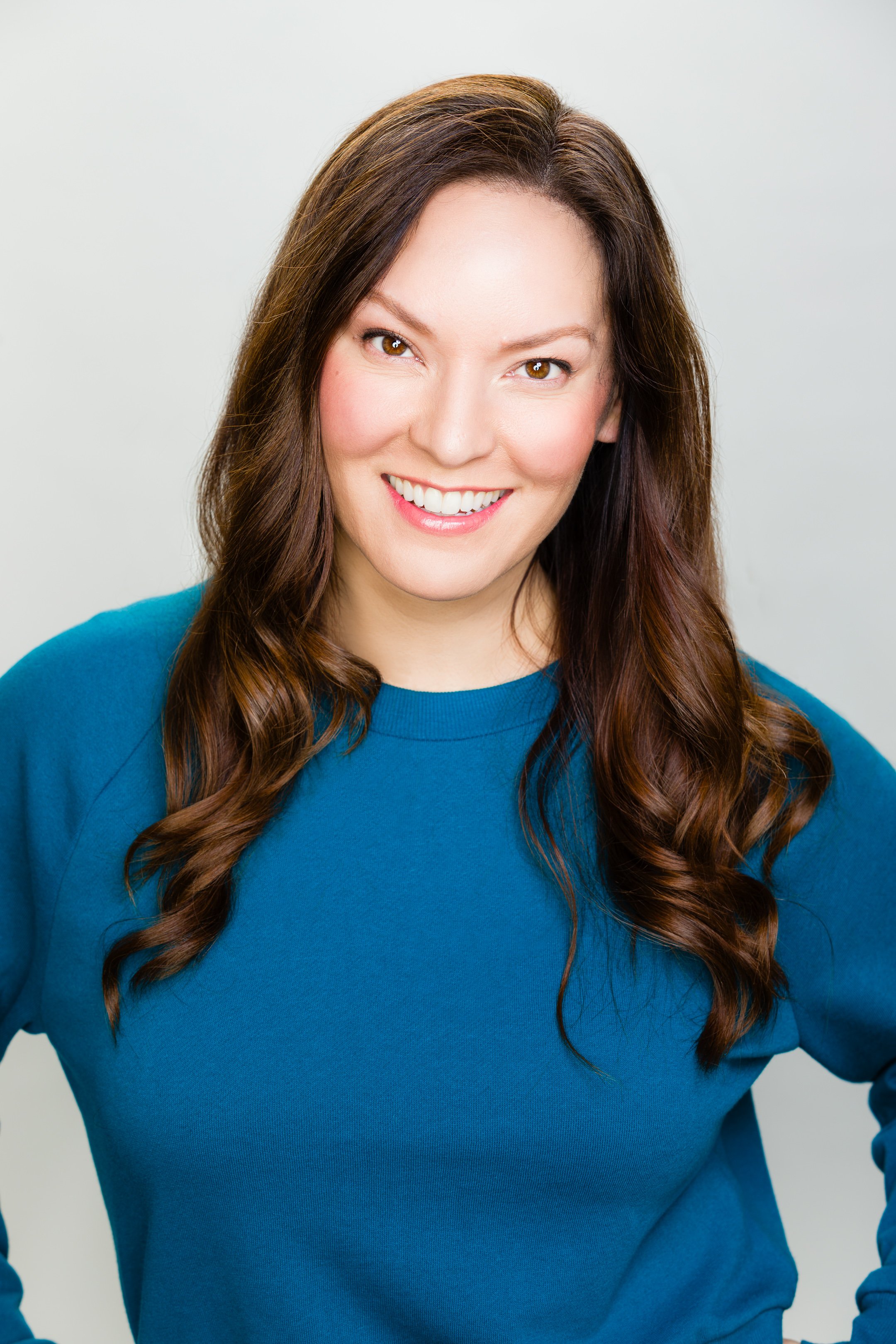 Sarah Claspell smiling and wearing a blue sweater, against a plain light background.