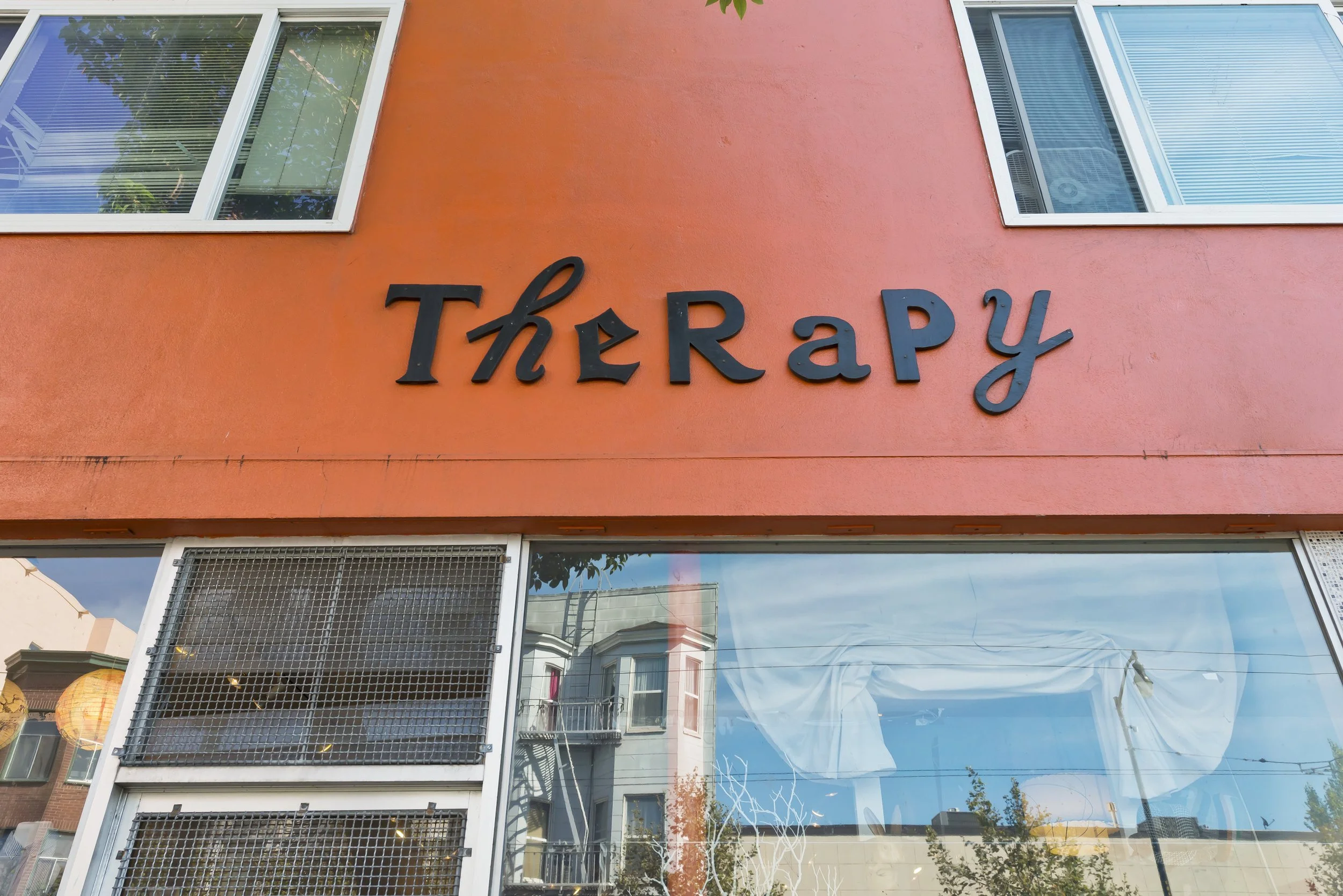 Front of a building with a pink exterior wall and large windows. The sign on the wall reads 'THERAPY' in black letters.
