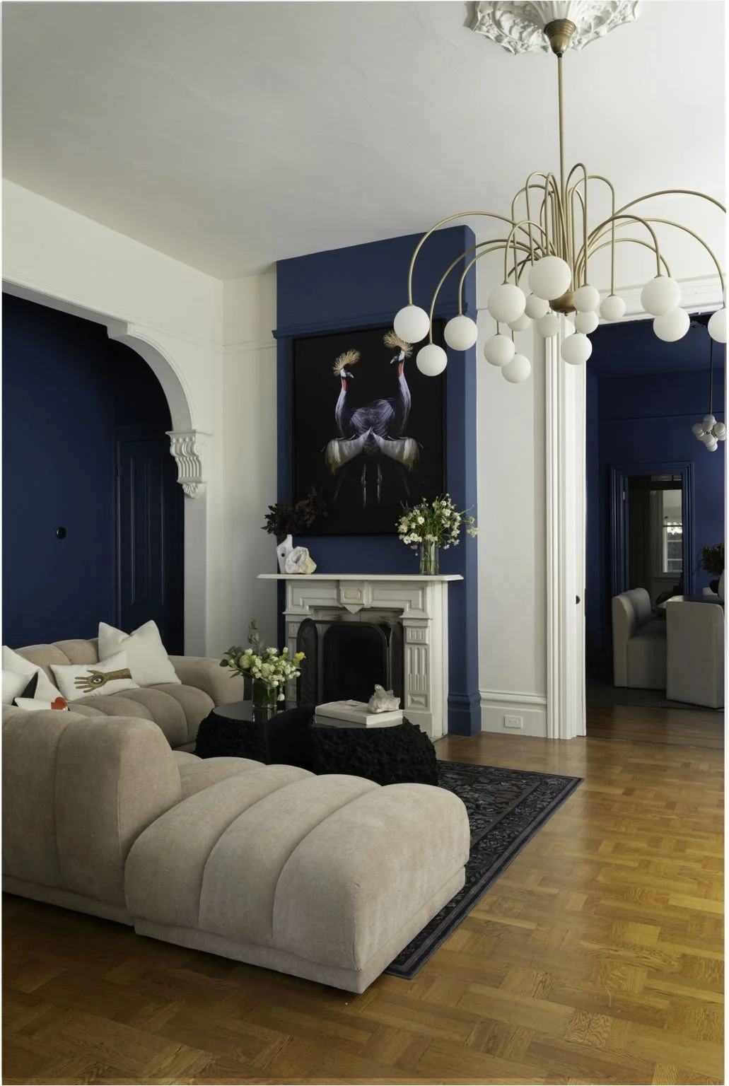 Living room with beige sectional sofa, black coffee table, white fireplace, blue walls, and a modern chandelier with white globes.