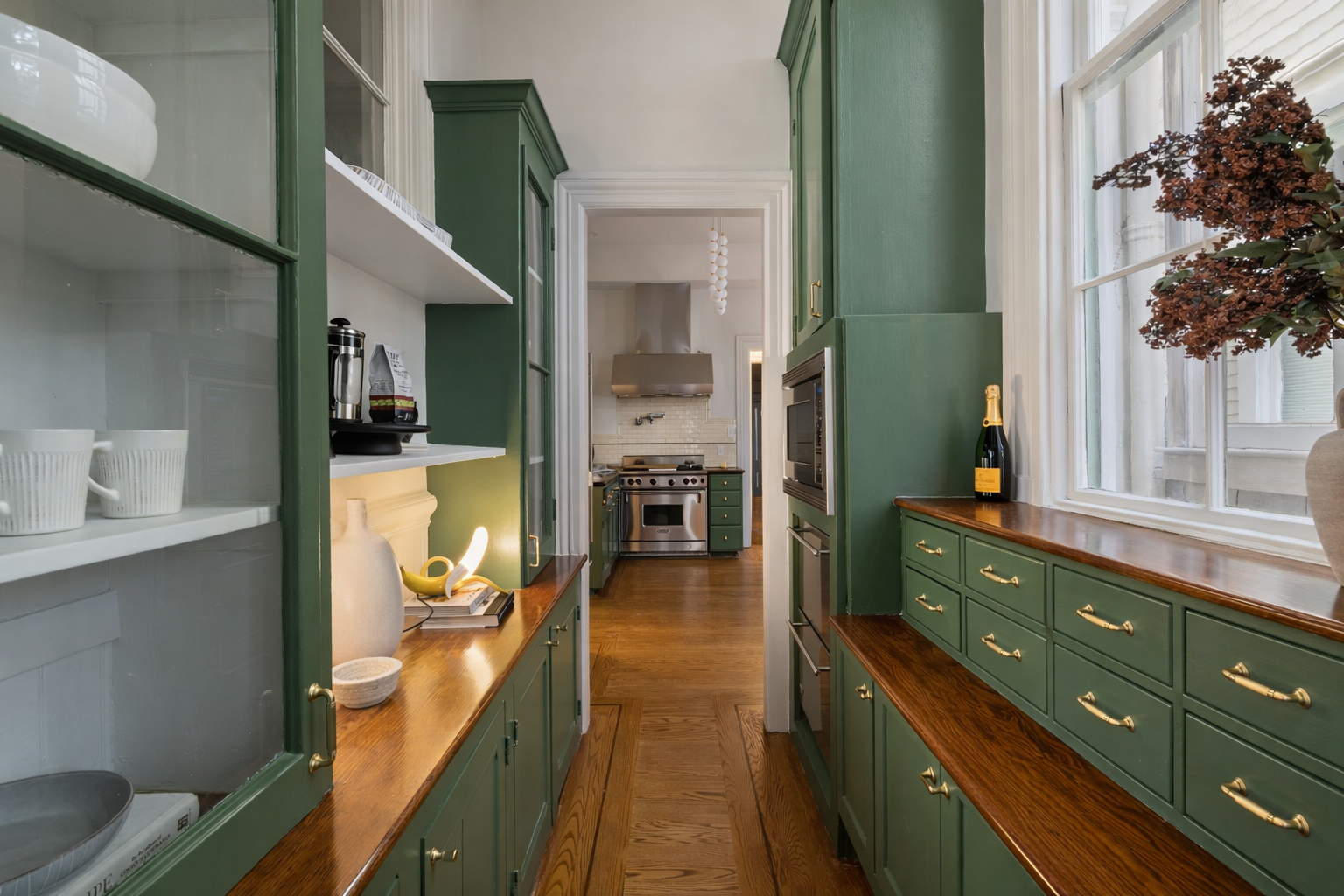 A kitchen with green cabinets, wooden countertops, and a view into the cooking area with stainless steel appliances and white backsplash.