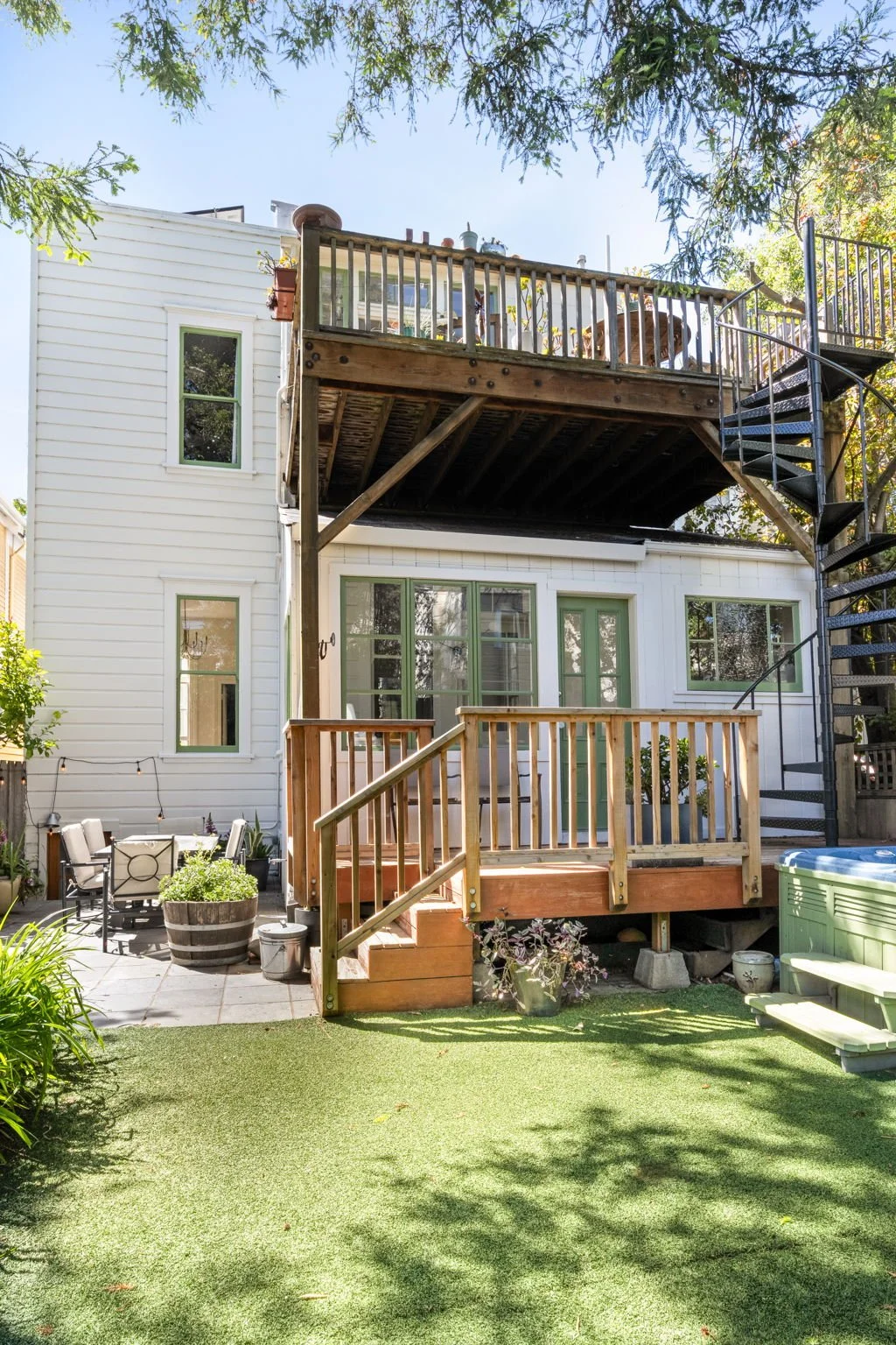Backyard patio with two-level deck, spiral staircase, outdoor dining area, potted plants, and landscaped grass area.