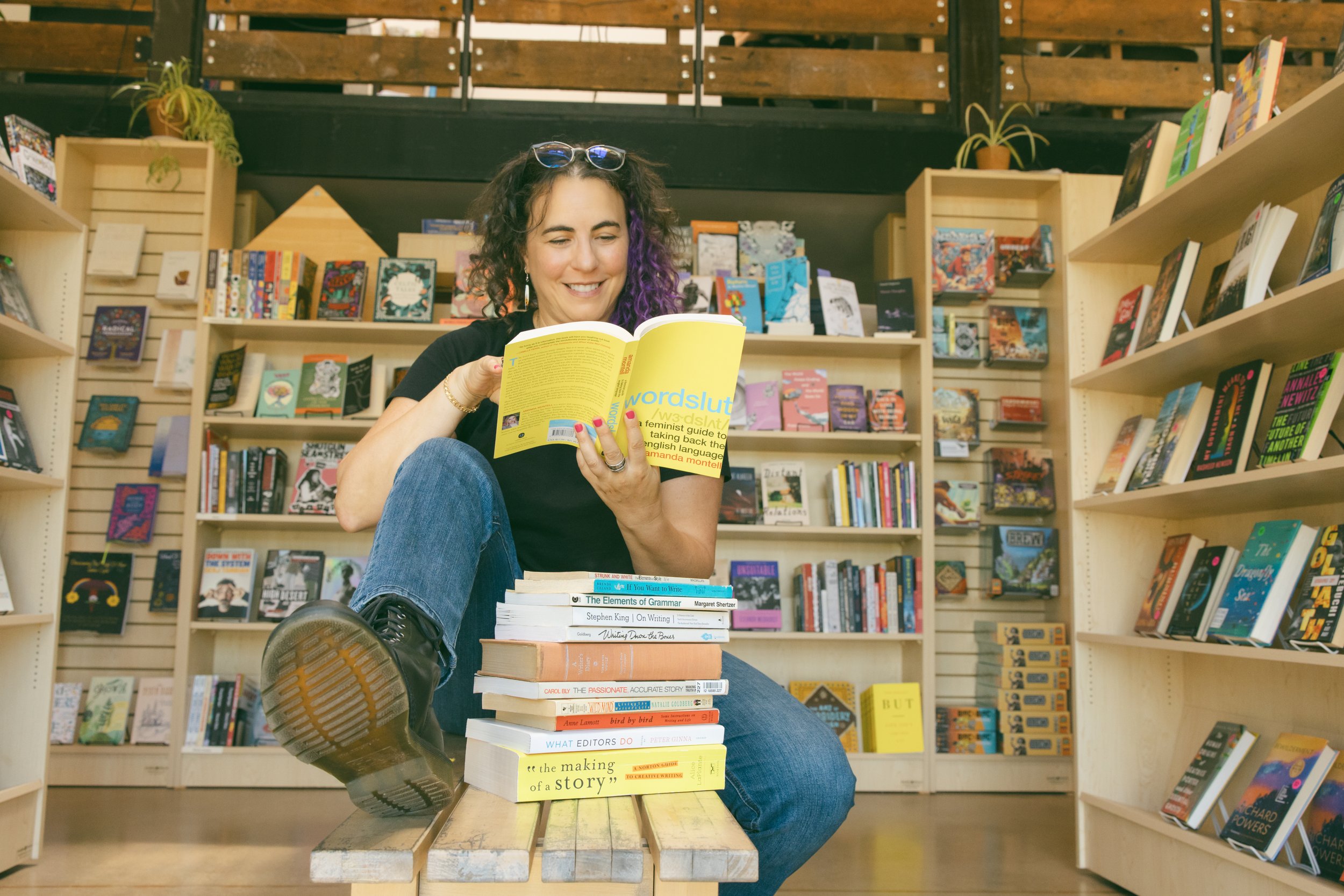 Samantha Pollack, writing coach and editor, sitting in a bookshop reading a book with a yellow cover
