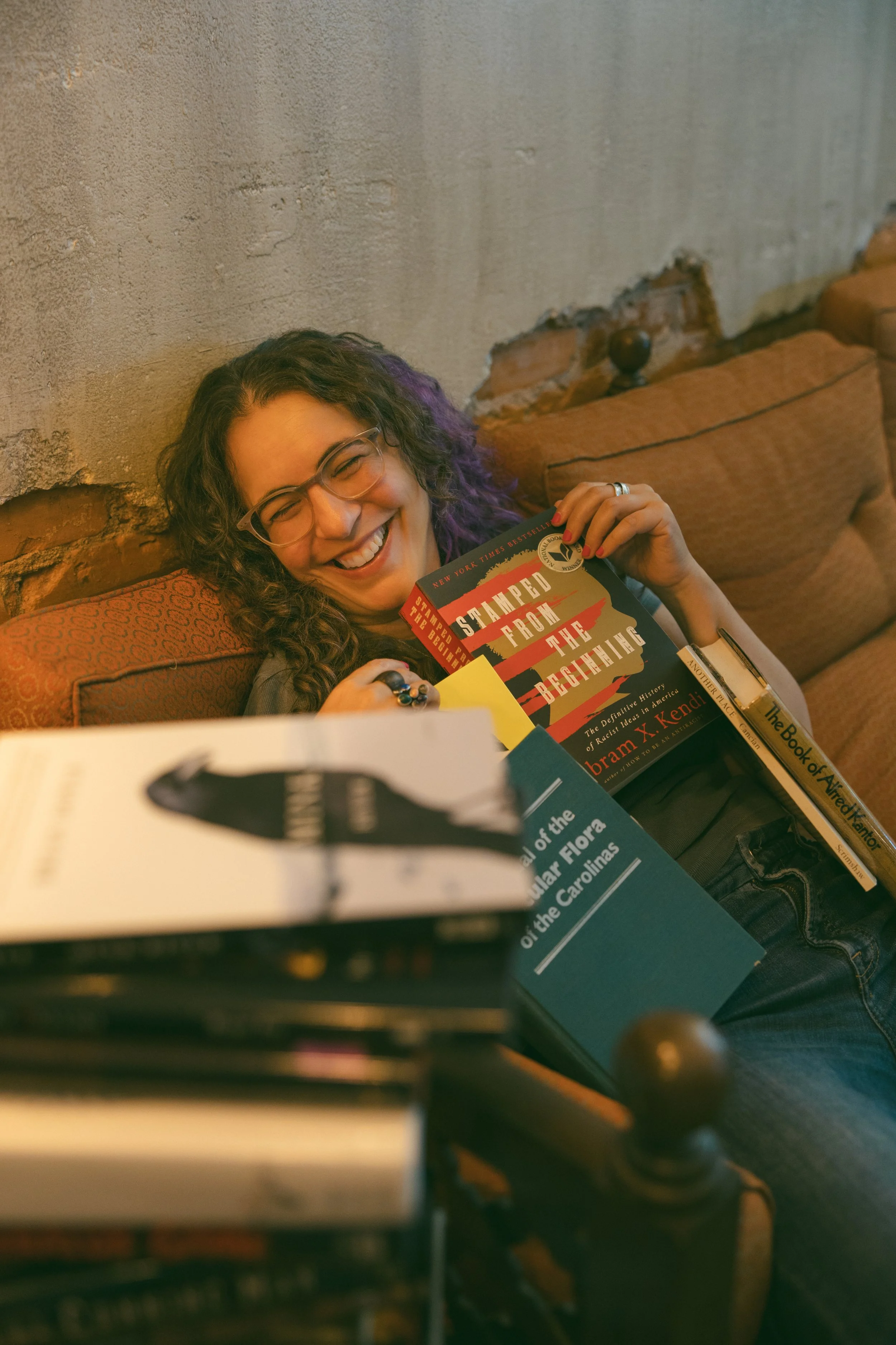 Samantha Pollack, Writing Coach and Developmental Editor, buried in a pile of books and laughing on a couch