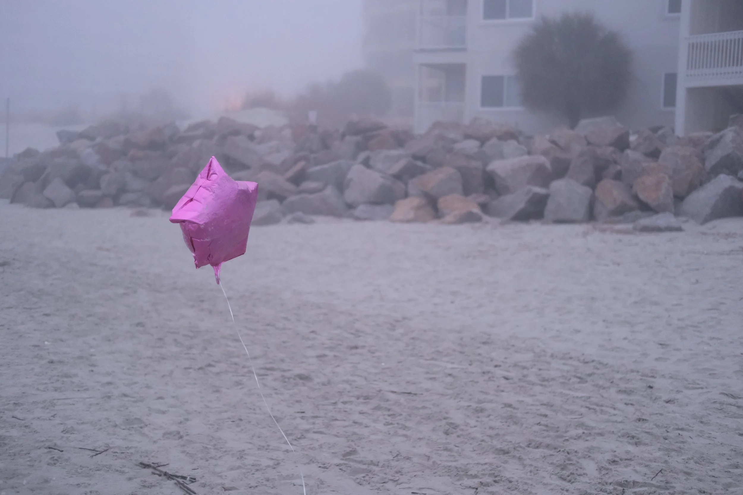 A pink mylar balloon on a misty grey beach