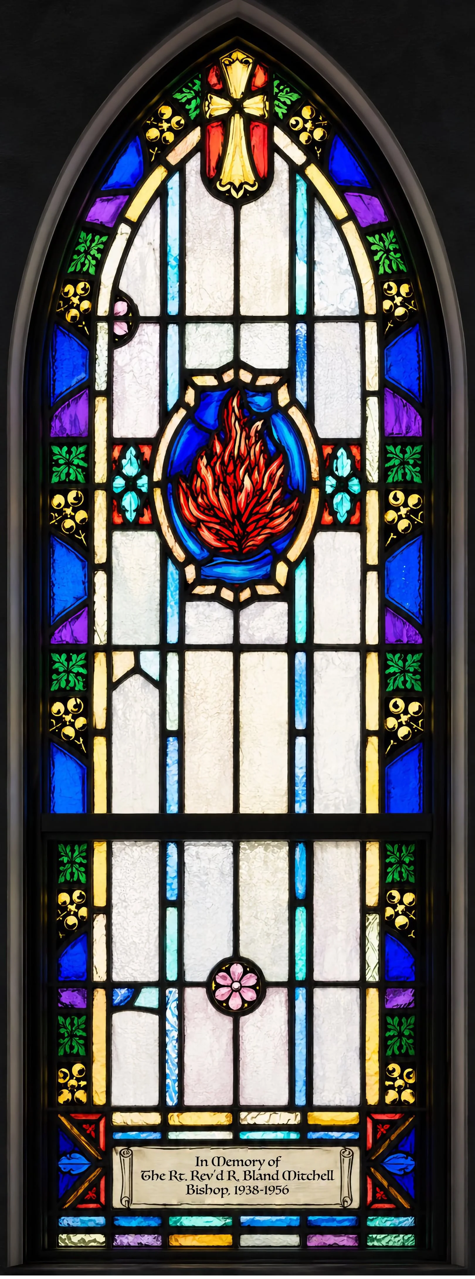 Pentecost (Epistle side, nearest the altar). A tongue of fire descends, as on the apostles at the birth of the Church (Acts 2:2–4). Given "In Memory of the Rt. Rev. R. Bland Mitchell, Bishop, 1938–1956" — fittingly, since Bishop Mitchell designed bot