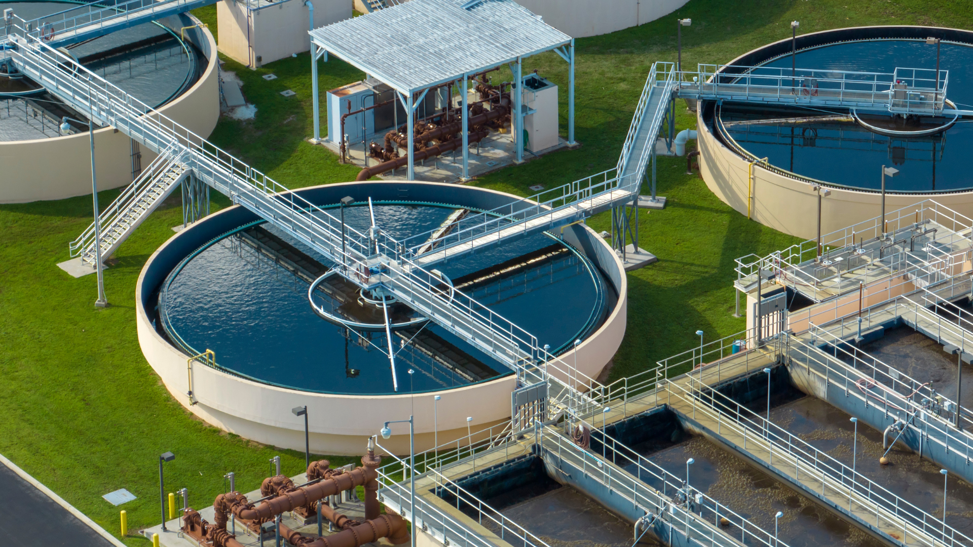 Tres tanques circulares de agua en una planta de tratamiento con tuberías y pasarelas de seguridad.