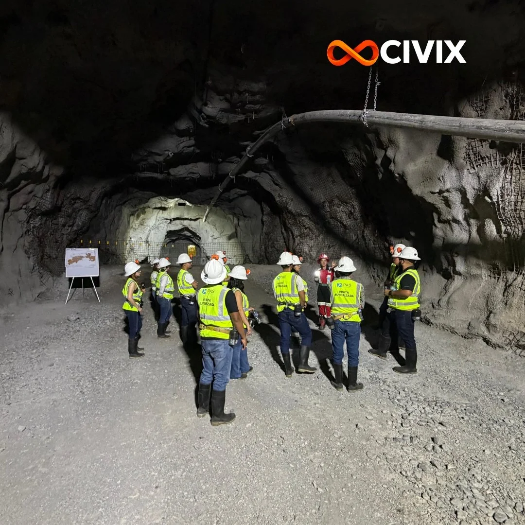 Grupo de personas con cascos y chalecos de seguridad en una mina subterránea, escuchando a un guía, con señalización y equipo técnico visible.