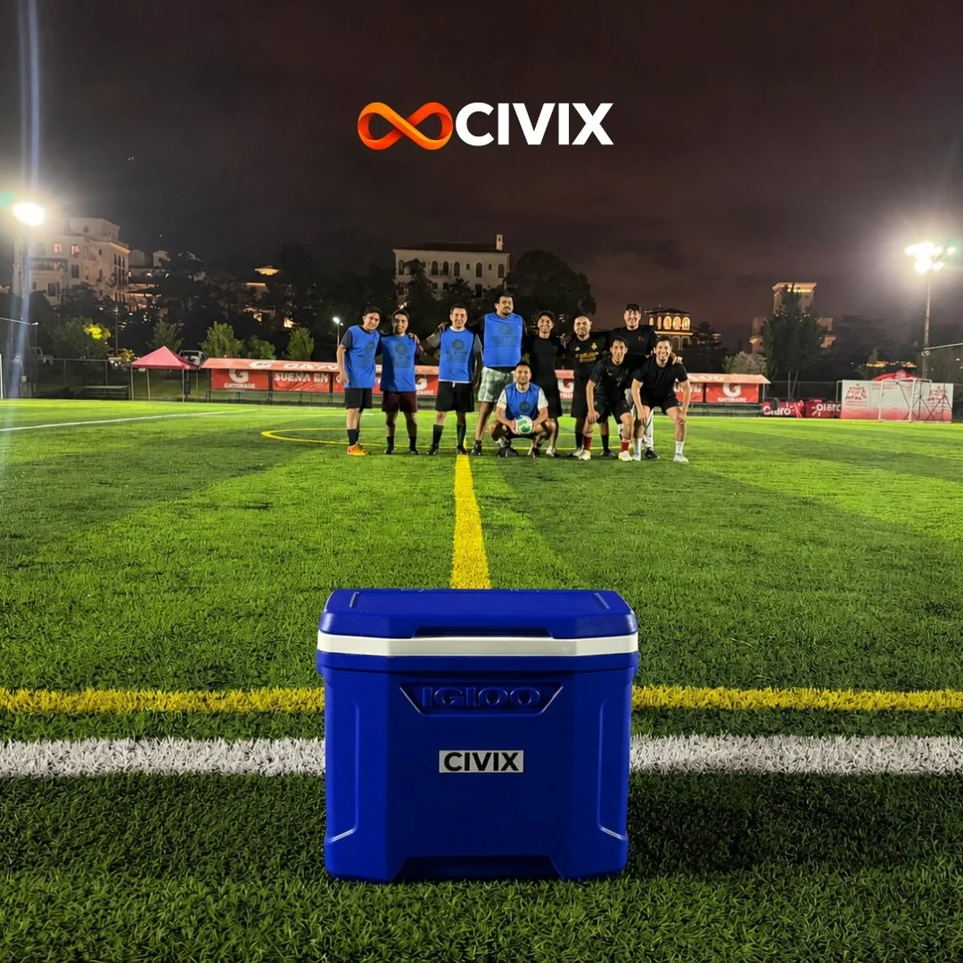 Grupo de jugadores de fútbol en un campo artificial, de noche, con un cooler azul frente a ellos y el logo de Civix en la parte superior del fondo.