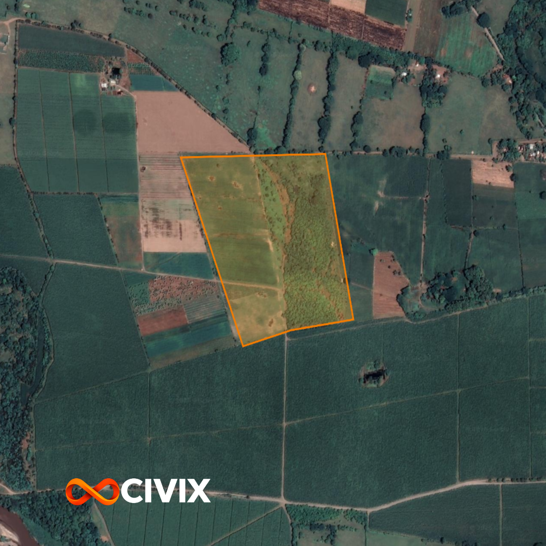 Vista aérea de un terreno agrícola delimitado con línea naranja, rodeado de diferentes cultivos y áreas verdes, con algunos caminos y pequeñas construcciones cercanas.