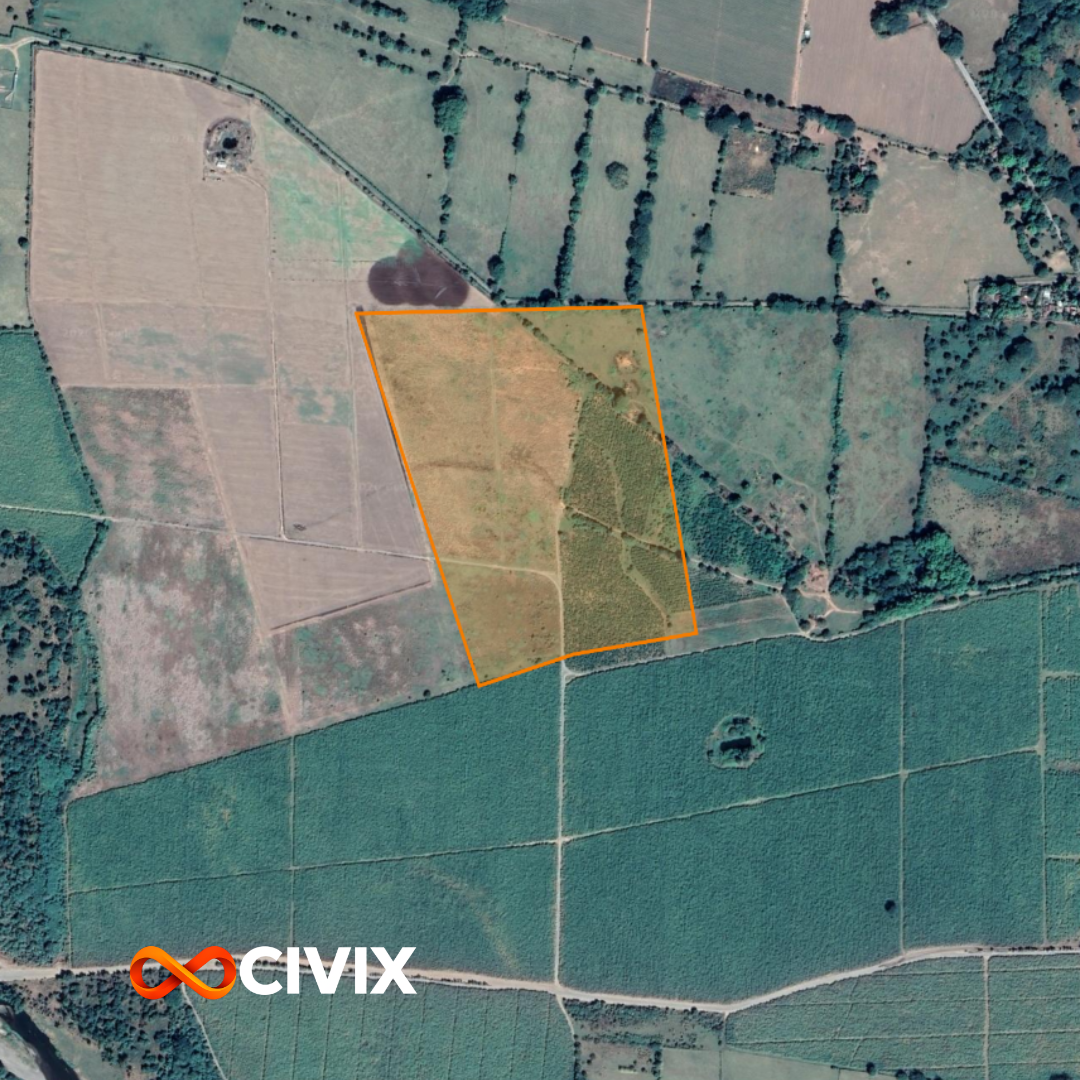 Imagen aérea de un terreno delimitado con línea naranja, rodeado de campos agrícolas y árboles, con caminos y parcelas rurales en la zona.