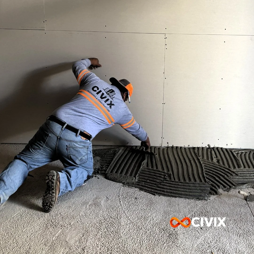 Trabajador de CIVIX extendiendo adhesivo con una llana dentada para instalar piso en un espacio interior.