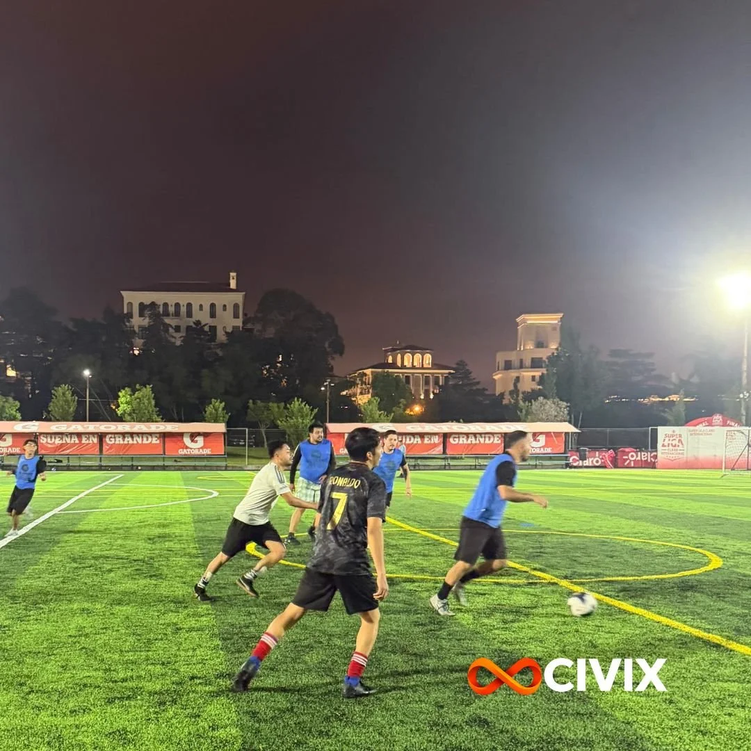 Niños jugando fútbol en un campo iluminado por la noche. Algunos llevan camisetas azules y uno con camiseta de Cristiano Ronaldo. En el fondo, edificios y árboles mientras el cielo está nublado. Logo de Civix en la esquina inferior derecha.