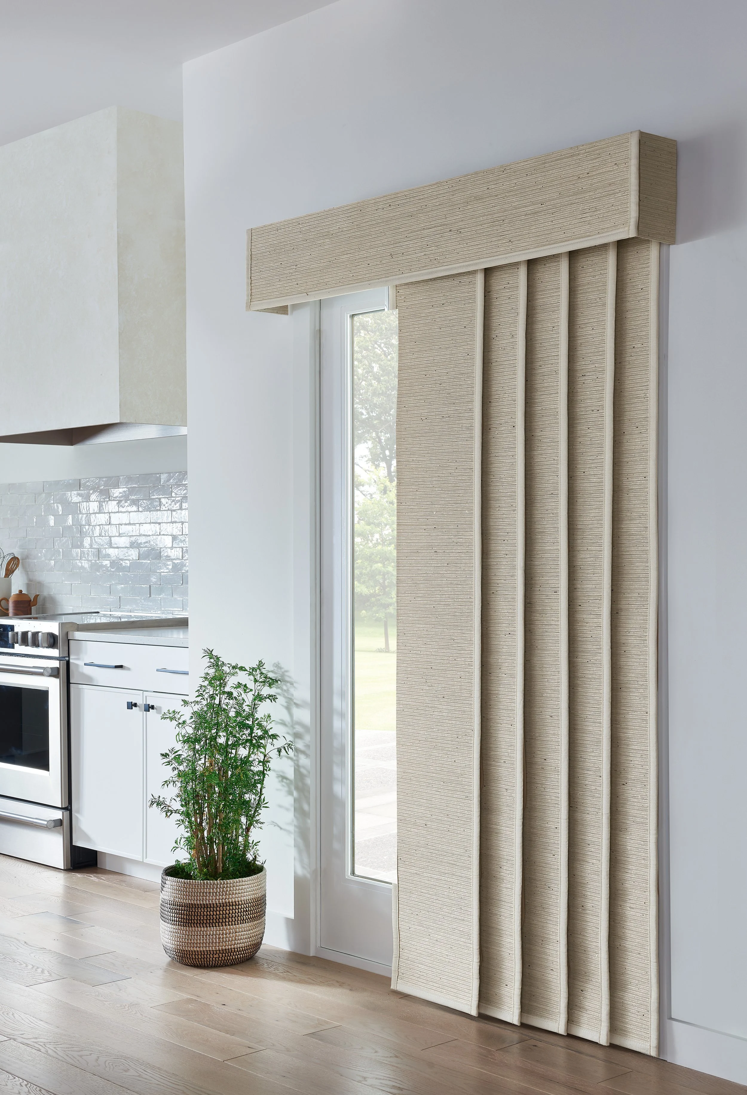 A beige customized acoustic panel with a textured fabric surface, designed as a decorative radiator cover, installed over a radiator next to a large window with natural light in a modern kitchen.