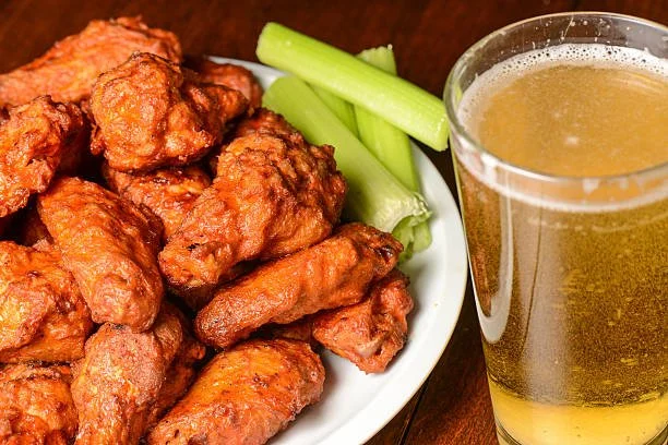 Fried chicken wings served with celery sticks and a glass of beer.