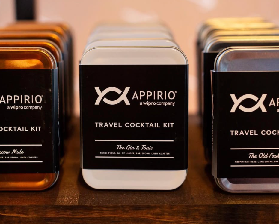 Metal tins labeled 'The Gin & Tonic' and 'The Old Fashioned' from Appirio travel cocktail kit, placed on a wooden surface.