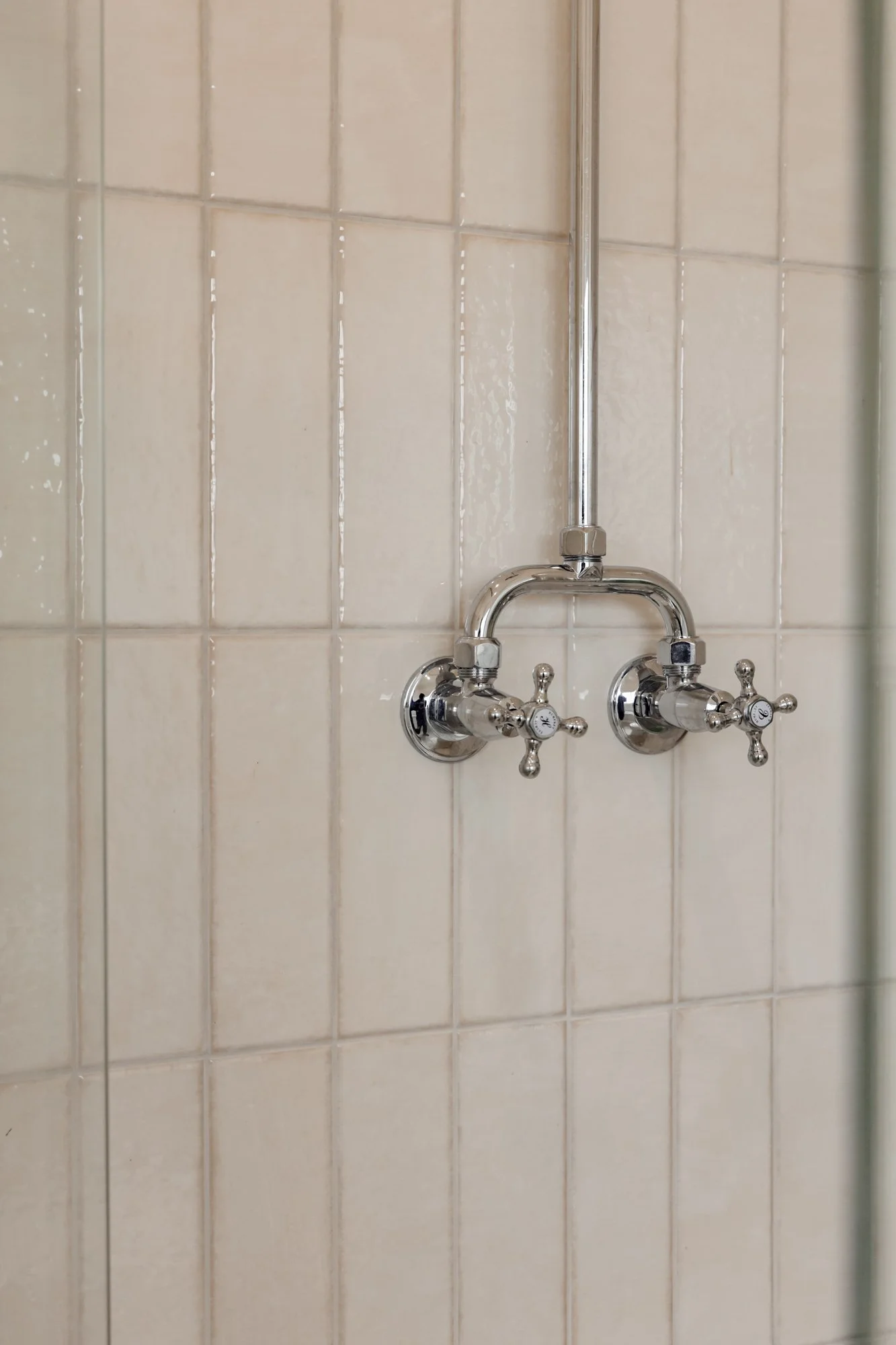 Close-up of a vintage-style dual water tap on a tiled wall.