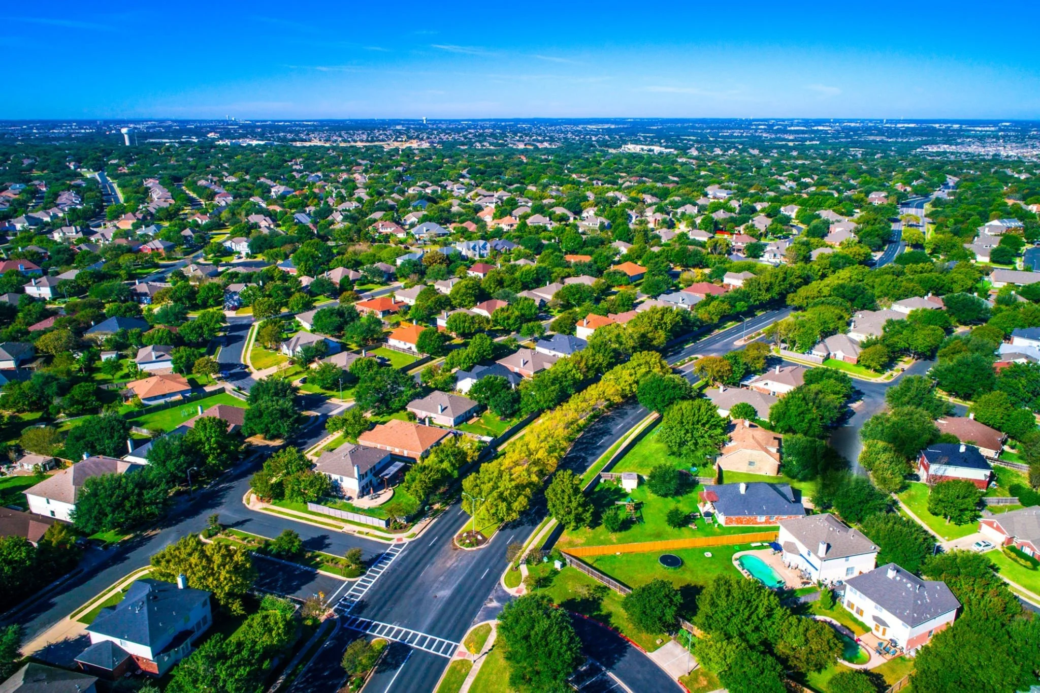 An aerial view of a suburban neighborhood with houses, trees, and curved roads, taken on a clear, sunny day.