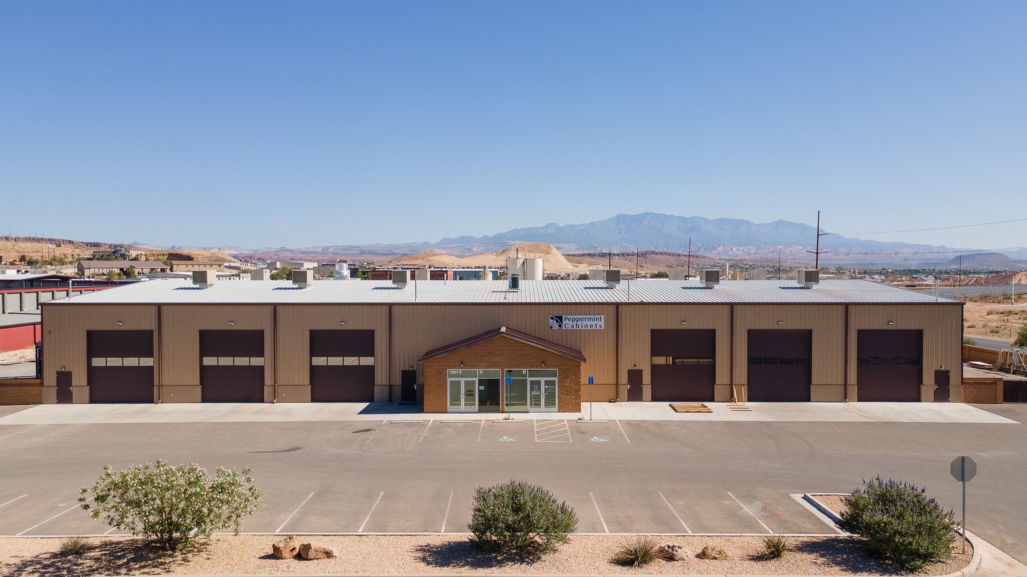 Industrial building labeled 'Peppermint Cabinets' with a parking lot and desert landscape with mountains in the background.