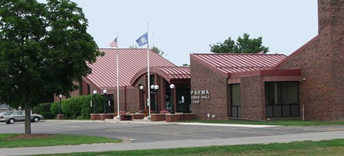 Front view of Parma City Hall building with its entrance, flags, trees, and parking lot