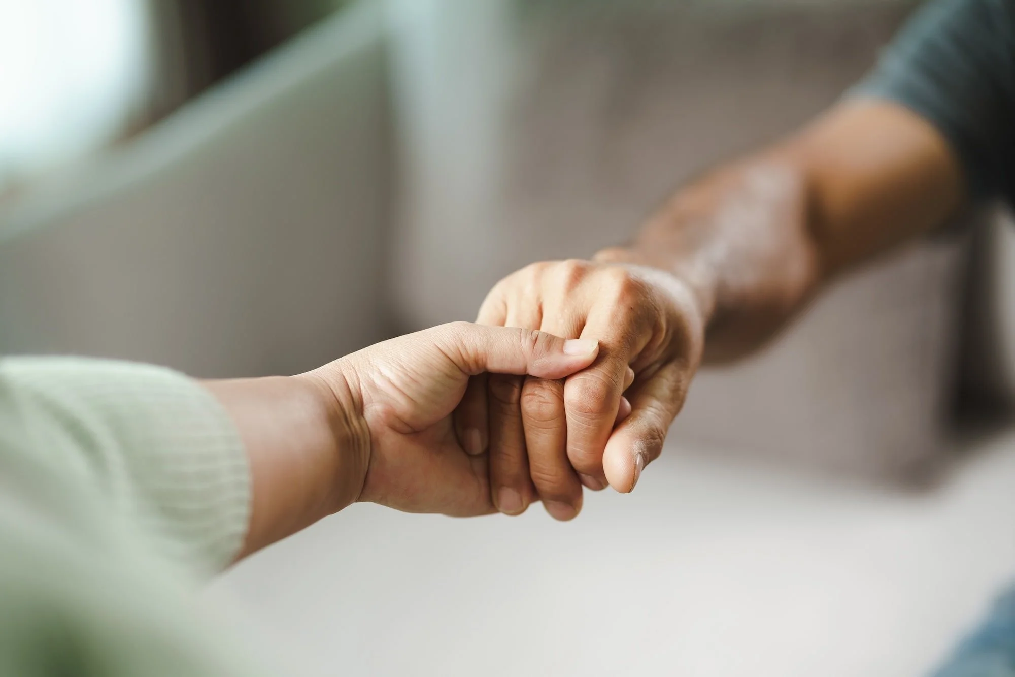 A close-up of a person holding an elderly person's hand, conveying care and compassion.