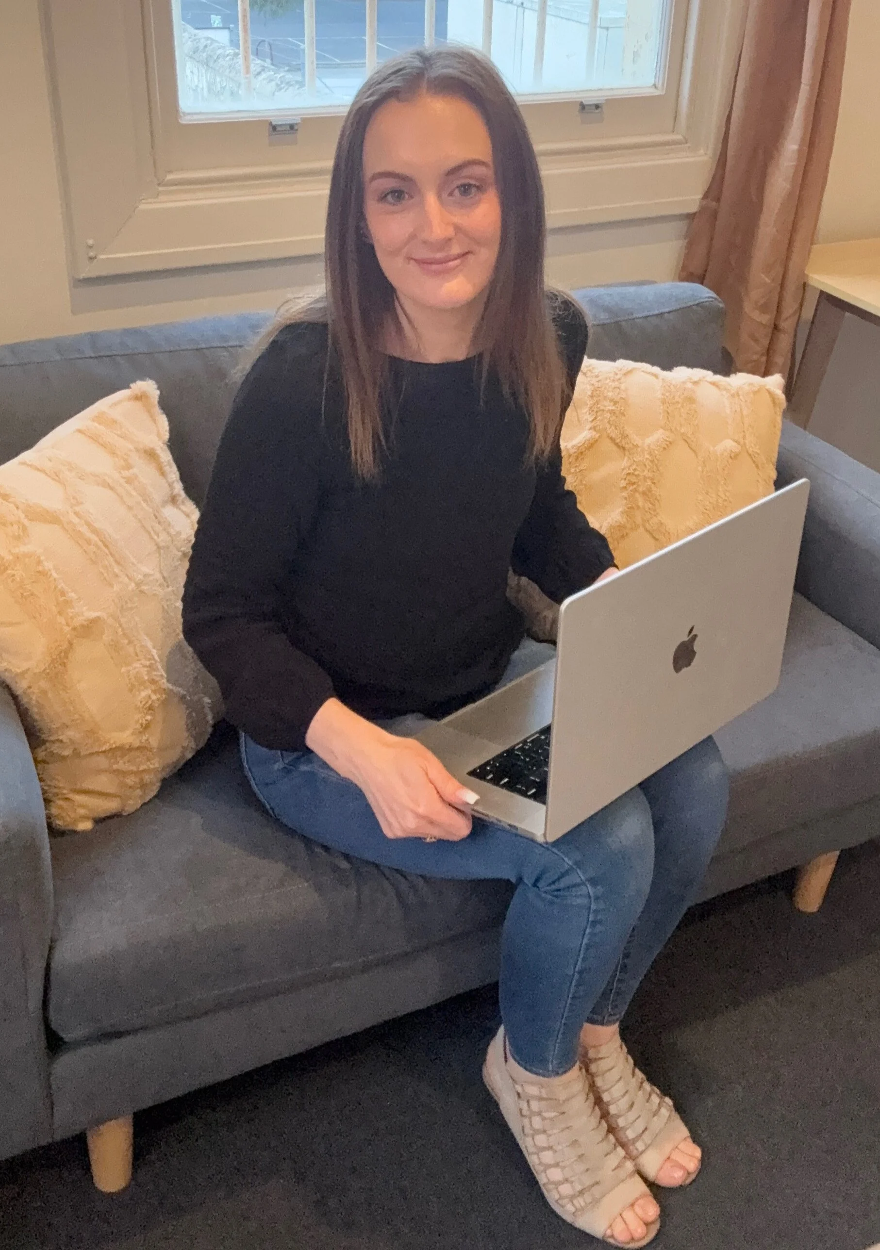 Jazmin Pursell, slight smile, sitting with laptop on couch in clinic