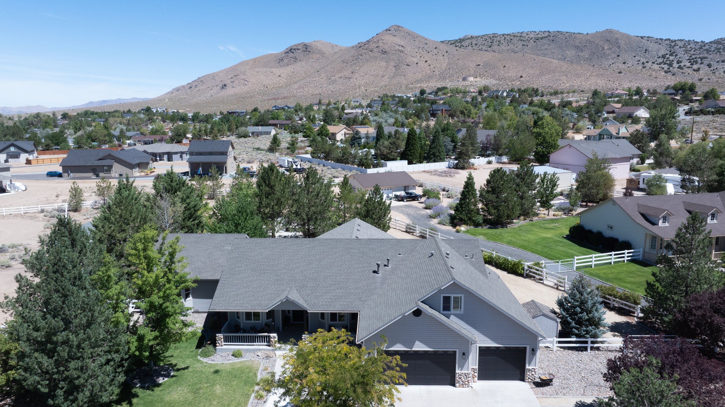 Aerial view of a suburban neighborhood with houses, trees, and mountains in the background.