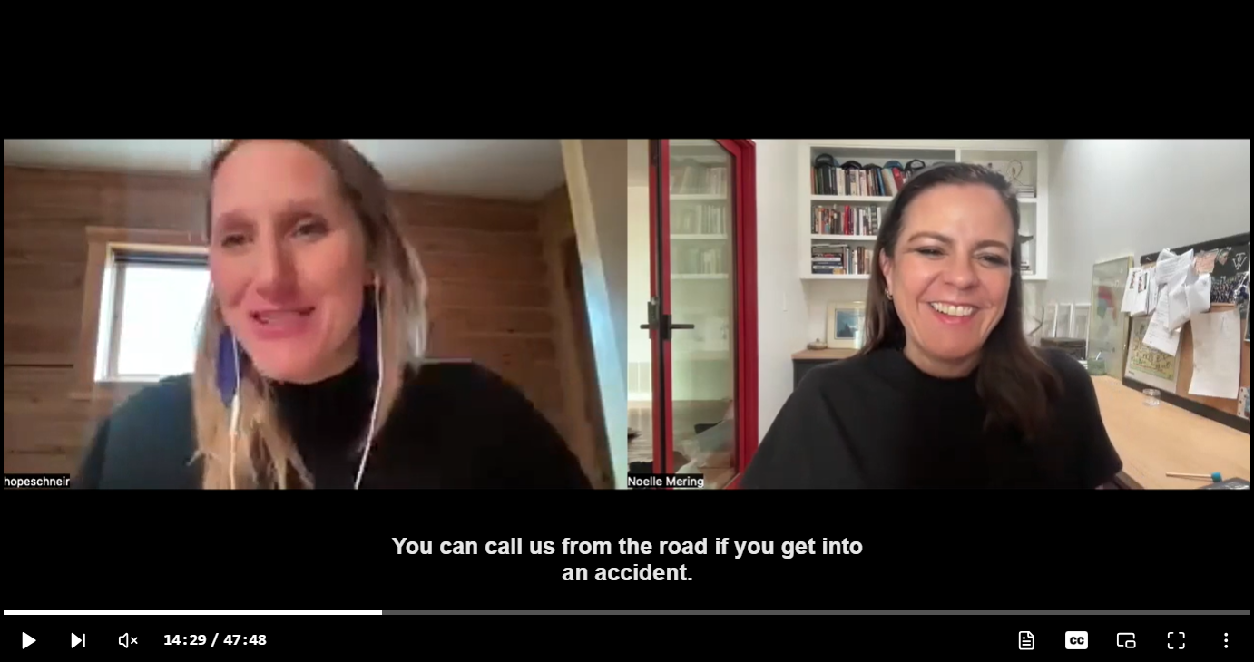 Two women are engaged in a video call, each in separate rooms. The woman on the left has long blonde hair, light skin, and is wearing a black top, headphones, and is in a room with wooden walls and a window. The woman on the right has medium-length dark hair, light skin, and is wearing a black top, with bookshelves, a red door, and a desk with papers behind her. The caption reads: 'You can call us from the road if you get into an accident.'