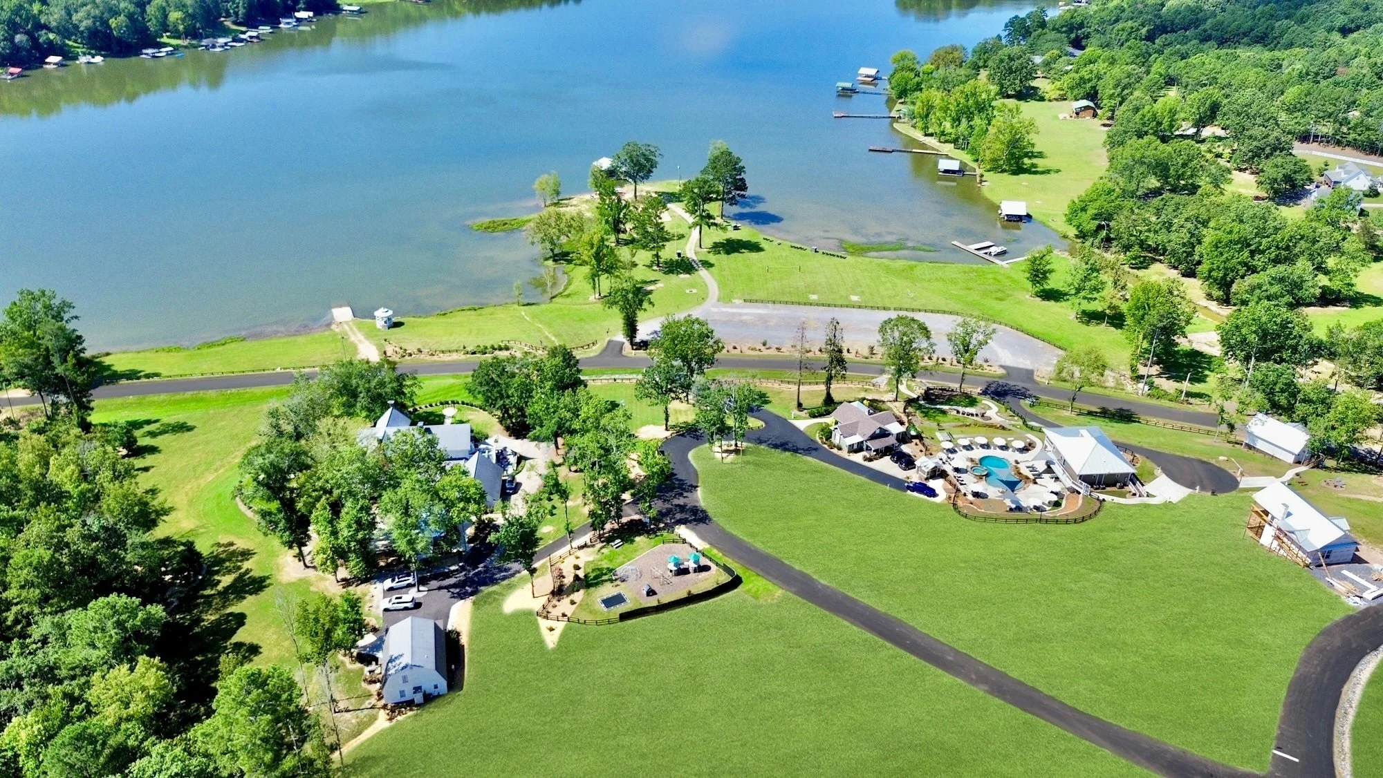 Aerial view of a lakeside community with houses, docks, boats, and green lawns surrounded by trees and water.