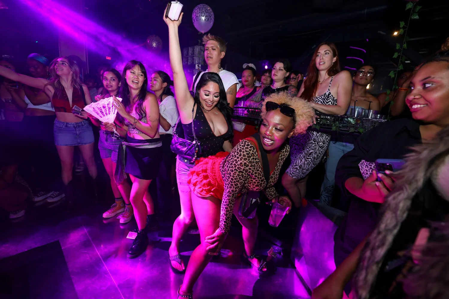Women dancing and having fun at a nightclub with purple lighting and balloons.