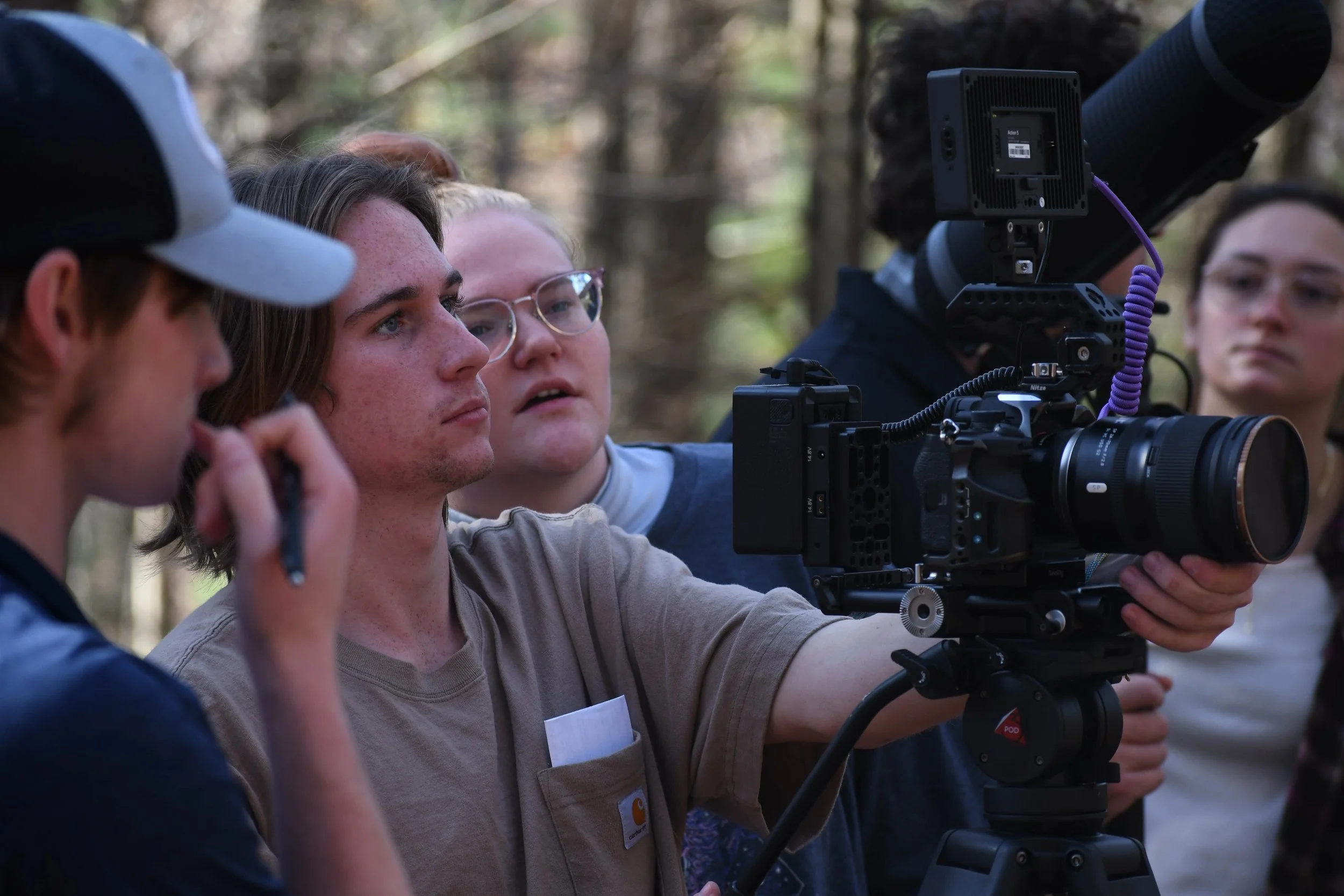 Group of young people working with a professional camera outdoors in a forest setting.