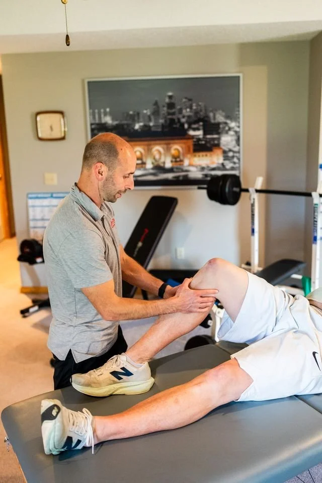 Physical therapist working with an elderly patient on leg rehabilitation in a home gym setting.
