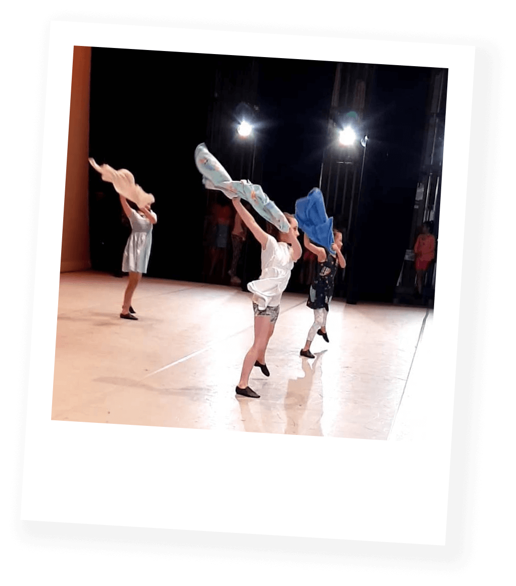 Children performing a dance on stage, swinging colorful scarves.