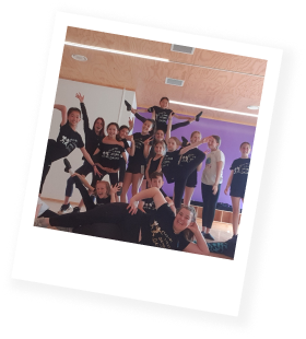 Group of people in a dance studio posing in various dance positions with some smiling and others in balance poses.